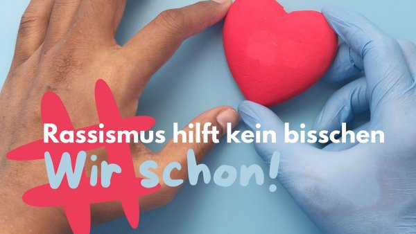 Eine dunkelhäutige Hand links sowie eine Hand in blauem Einweghandschuh rechts halten zusammen ein rotes Herz (blauer Hintergrund), darauf der Slogan der Kampange #RassismusHilfKeinBisschen - Wir schon!