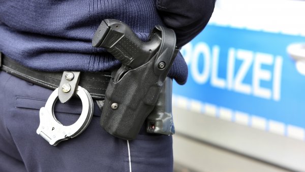 Polizist mit Waffe vor Polizeiwagen